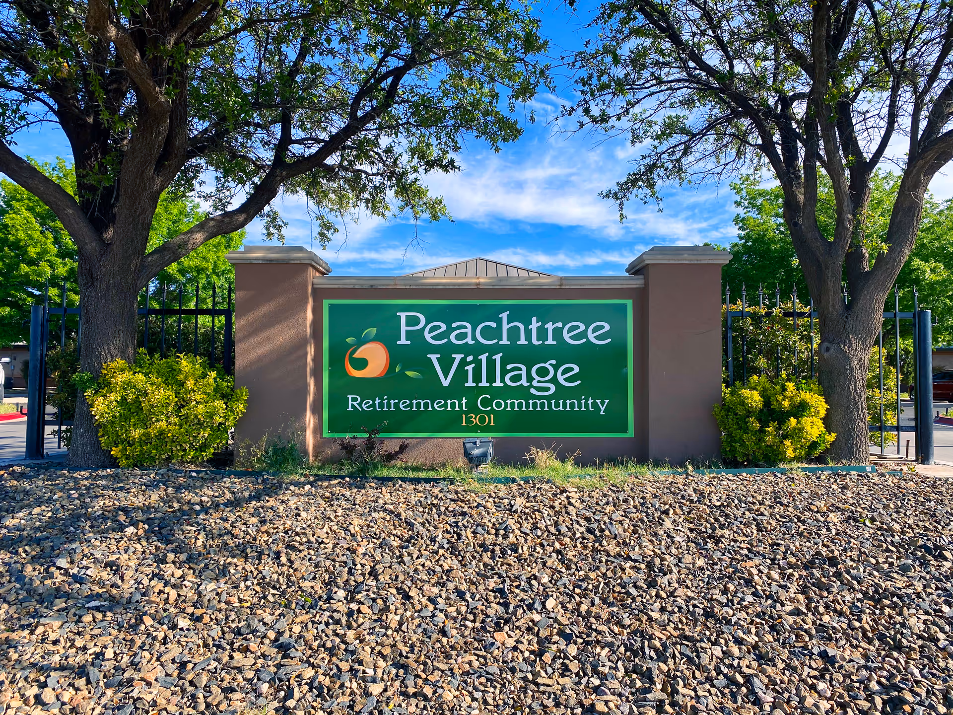 A green Peachtree Village Retirement Community sign framed by trees at entrance