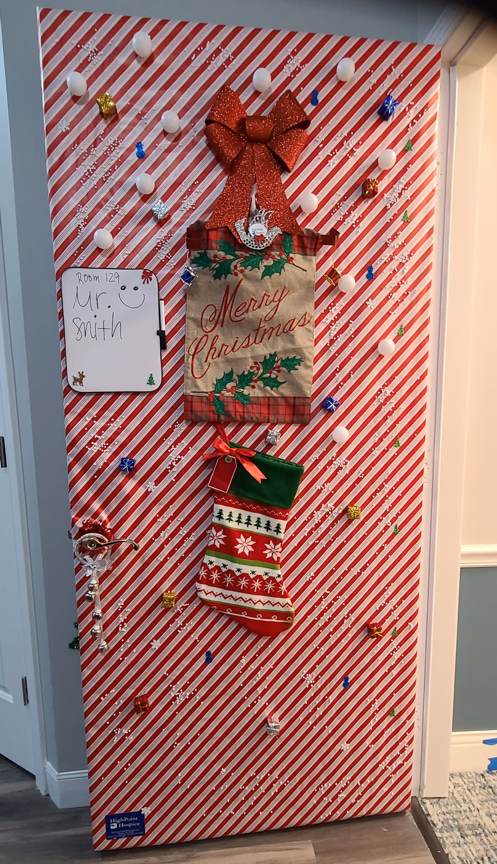 Interior hallway door festooned with red-and-white stripes, bow, stocking, and whiteboard.