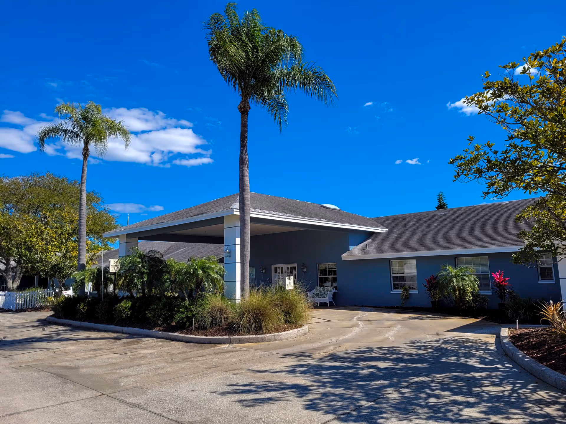 Exterior view of Sweet Water at Largo entrance with blue walls, palm trees, and driveway.