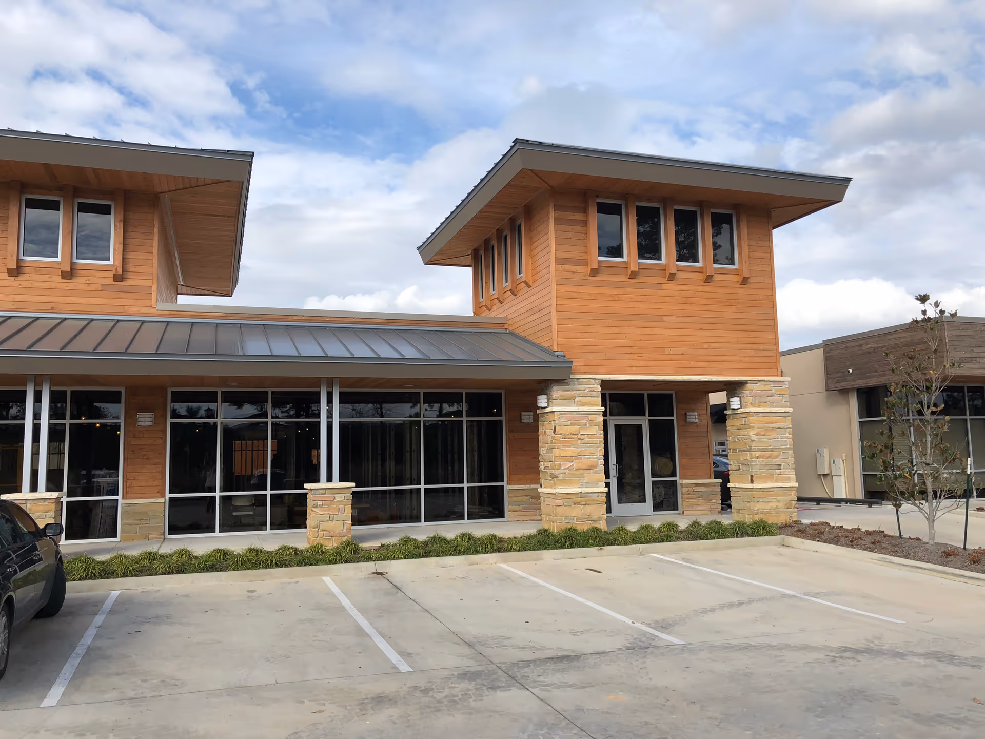 Front view of a modern medical office building with wood siding, stone columns, and glass storefronts.