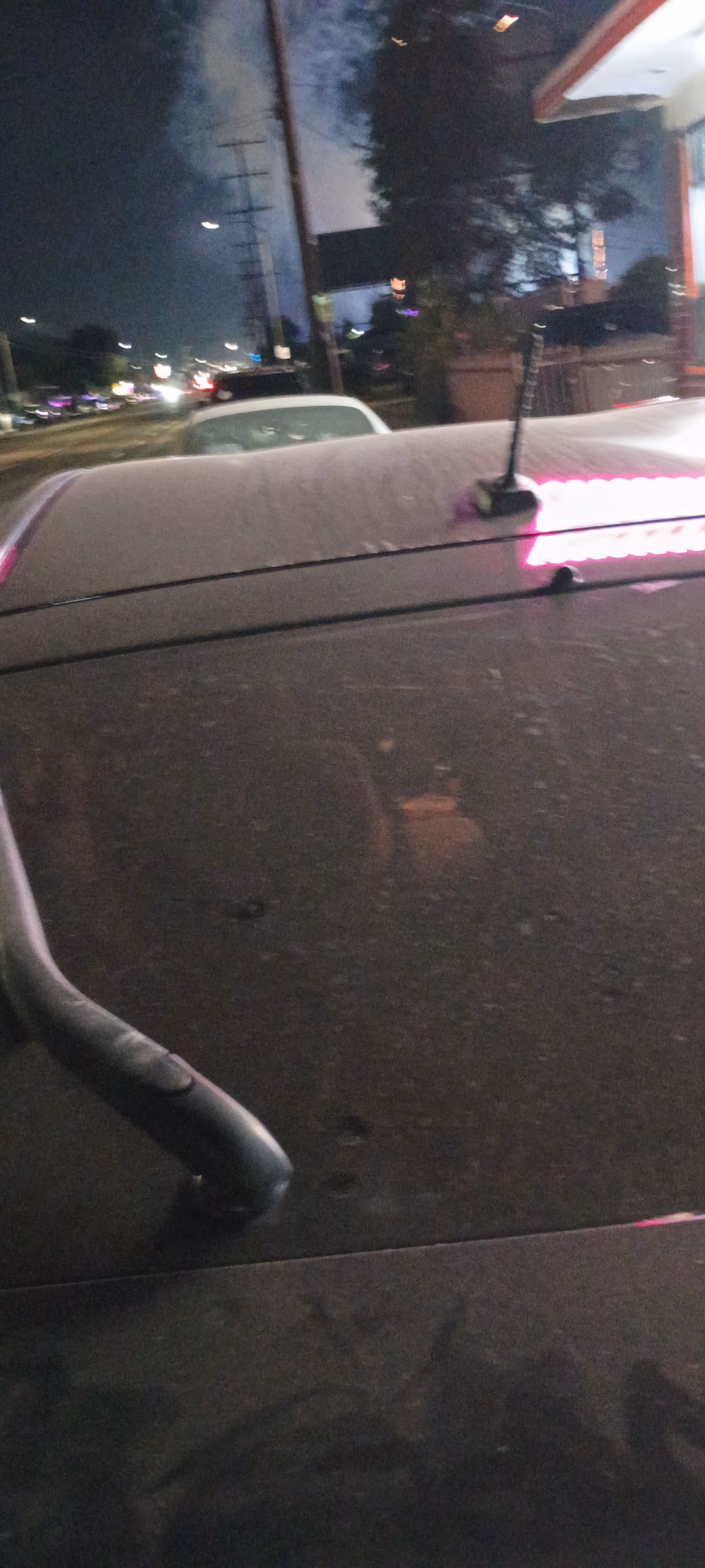 Nighttime exterior street scene showing a vehicle roof with pink lights.