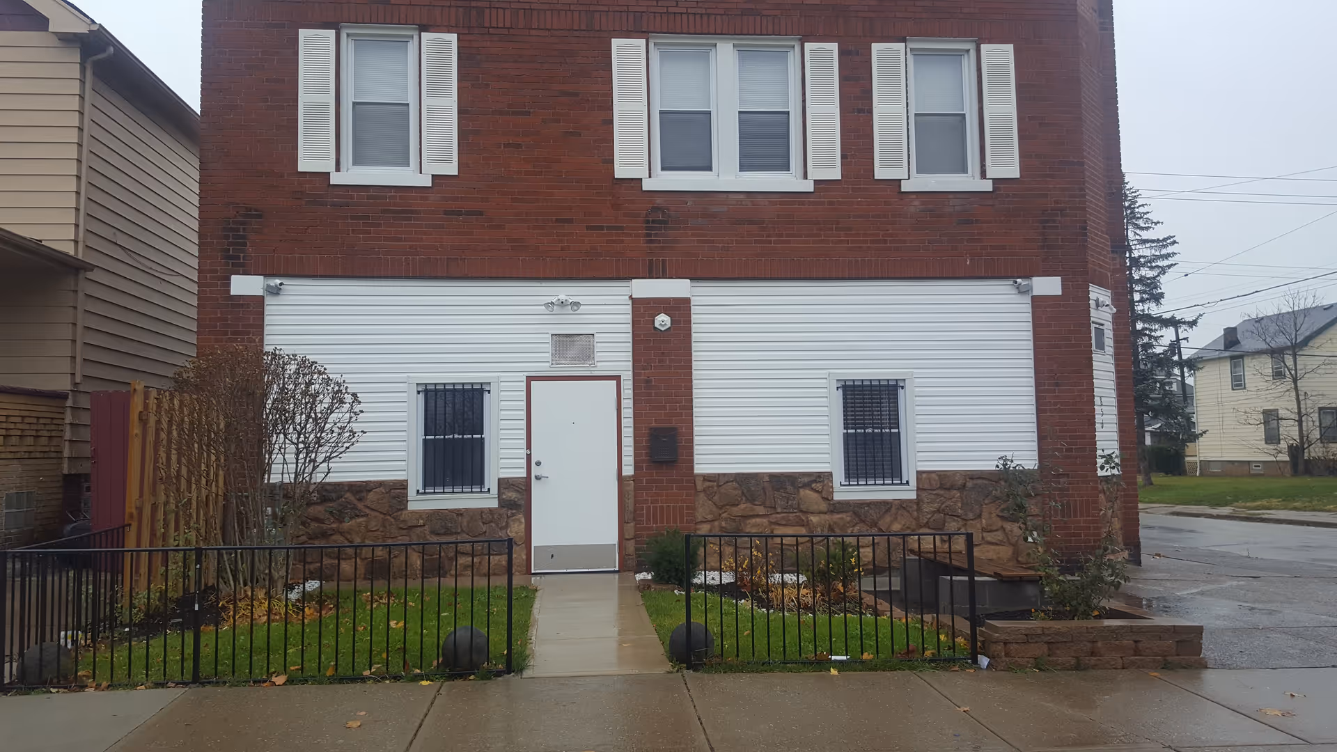 Brick building with white shutters and large white rolling doors, small front yard, sidewalk