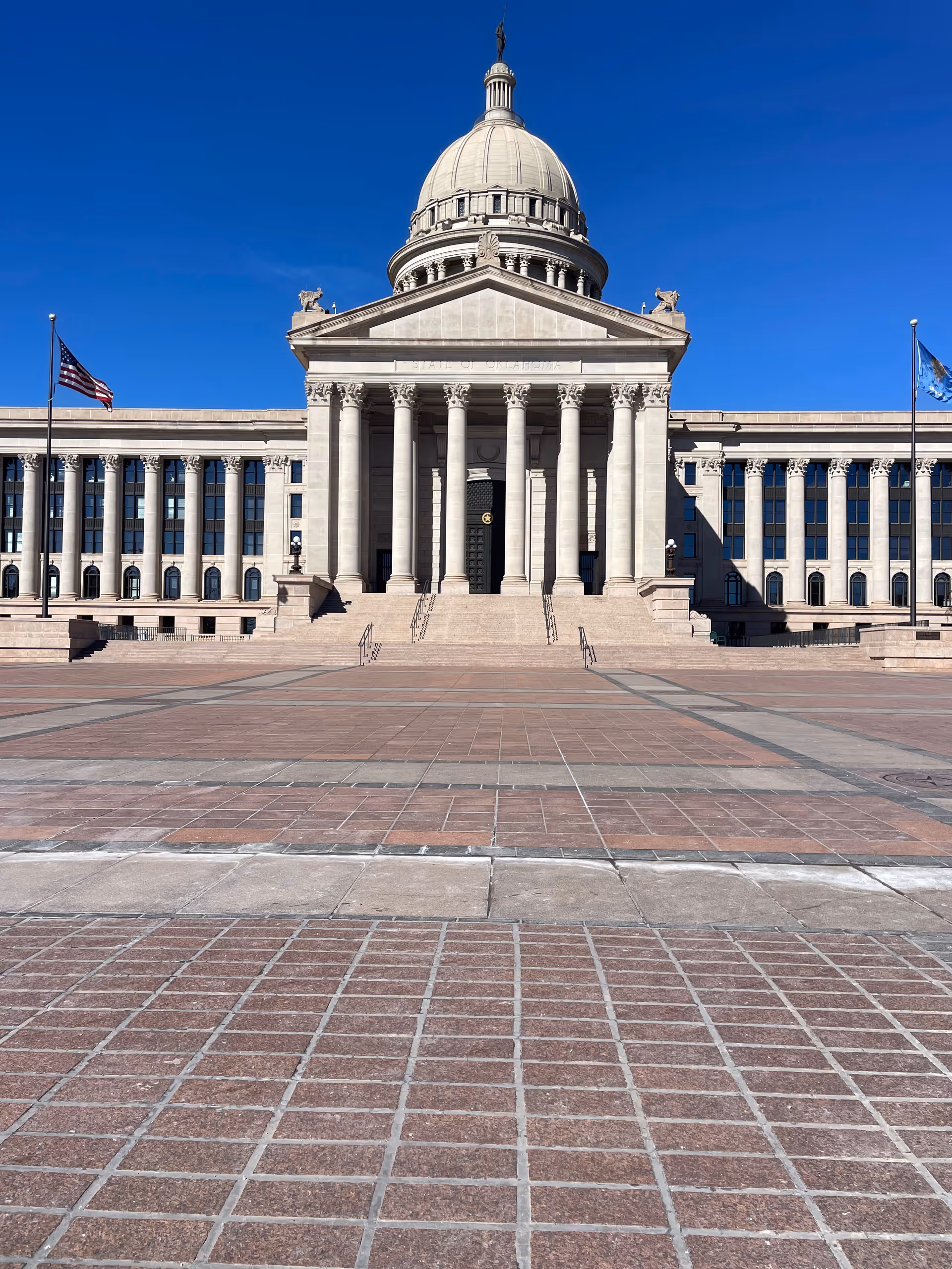 Grand neoclassical government building with a domed roof, tall columns, and flagpoles on a wide plaza.