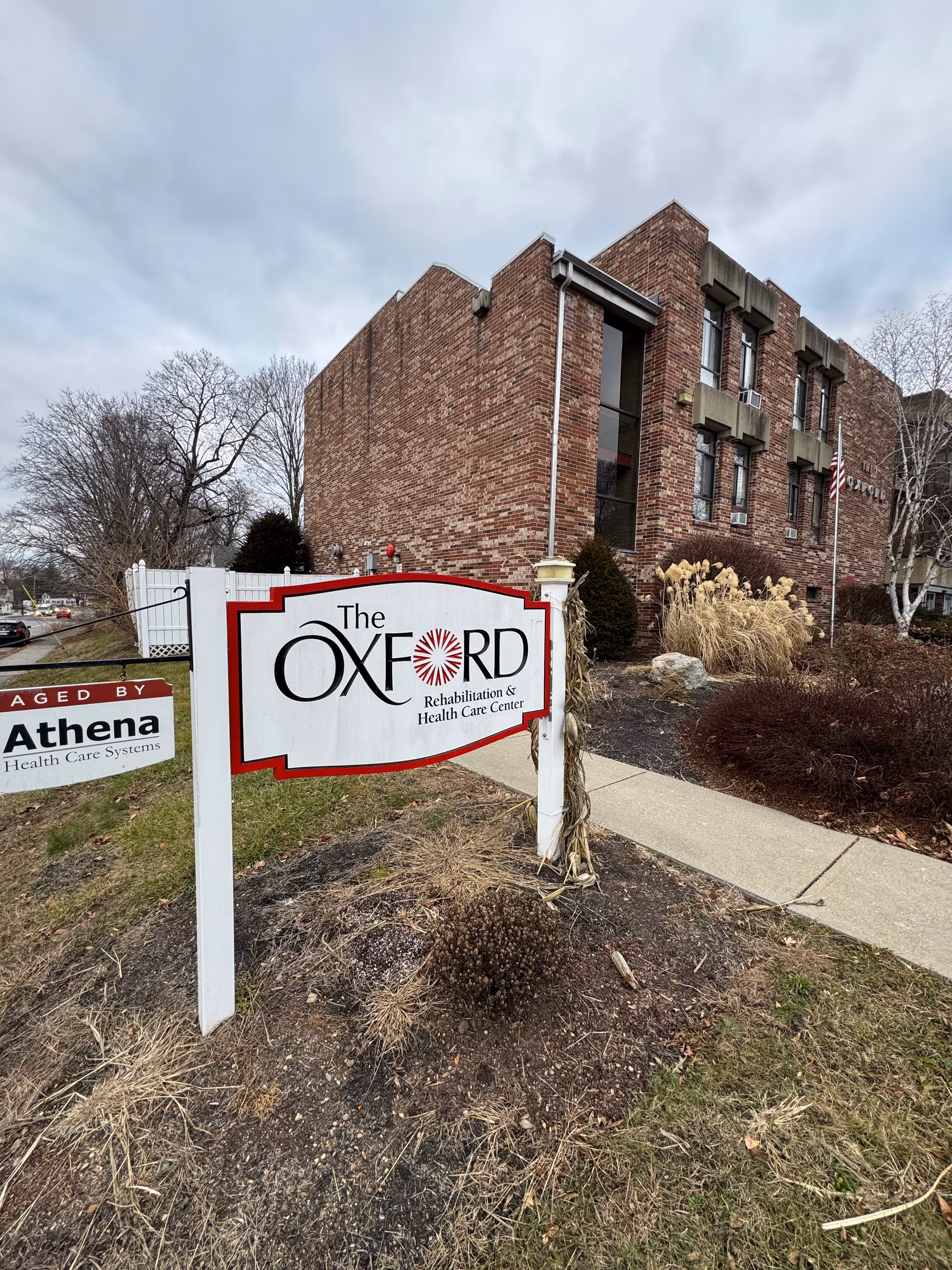 Exterior brick building with a sign for The Oxford Rehabilitation & Health Care Center near sidewalk