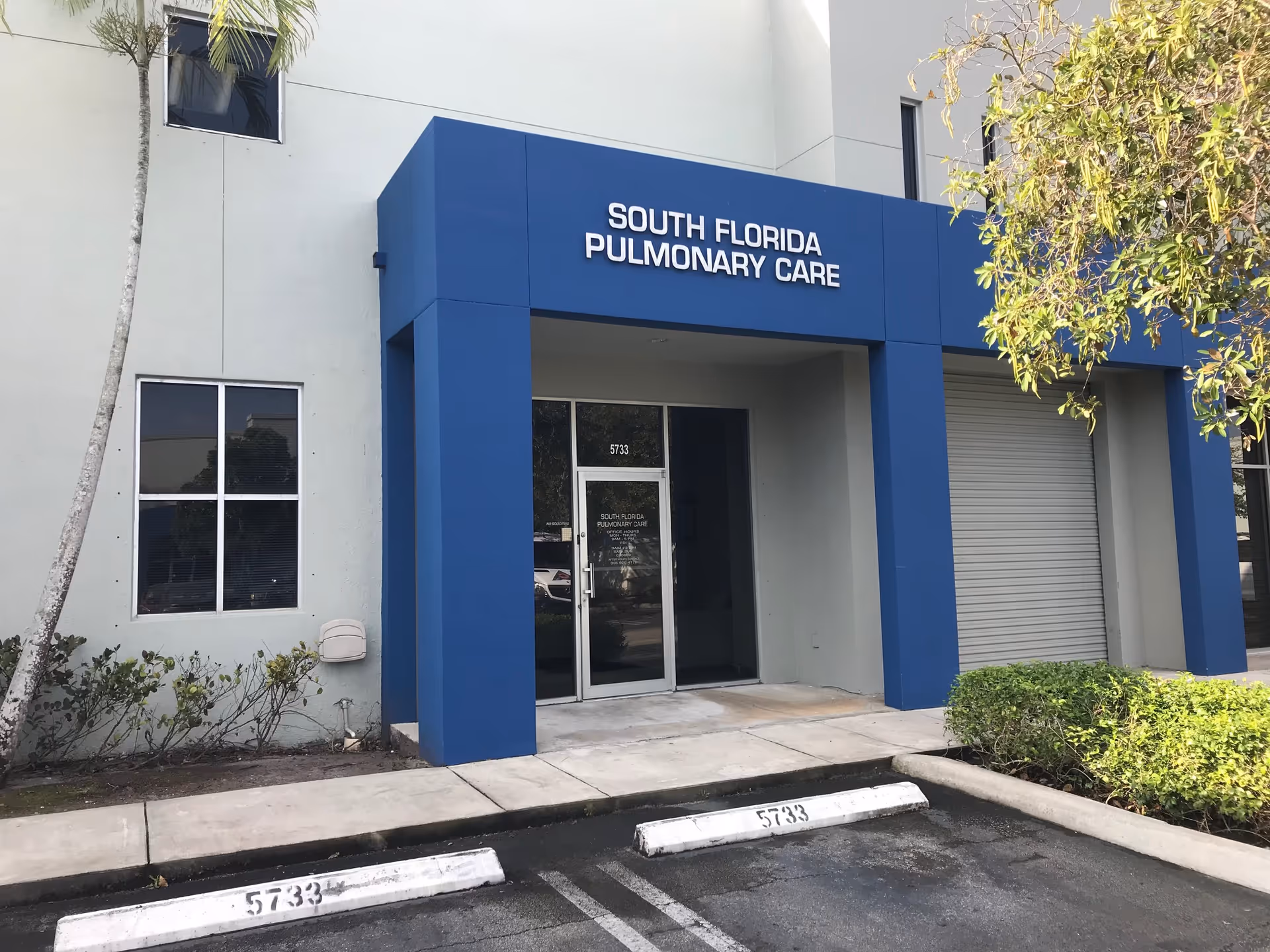 Exterior view of South Florida Pulmonary Care entrance with blue pillars and parking.
