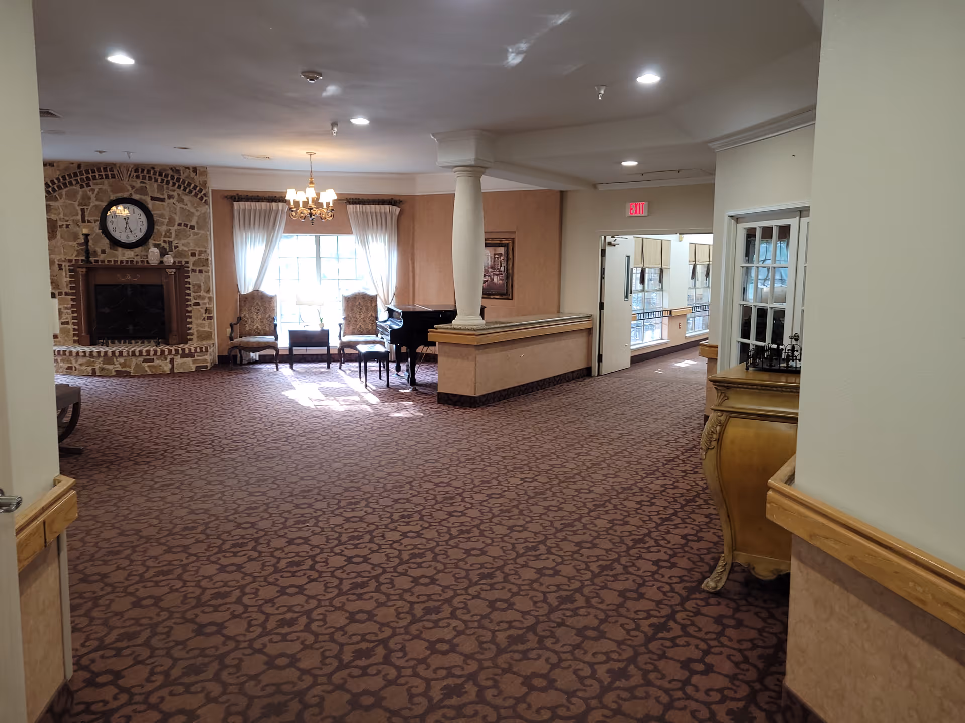Senior living facility lobby with fireplace, chandelier, piano, chairs, windows, and carpet