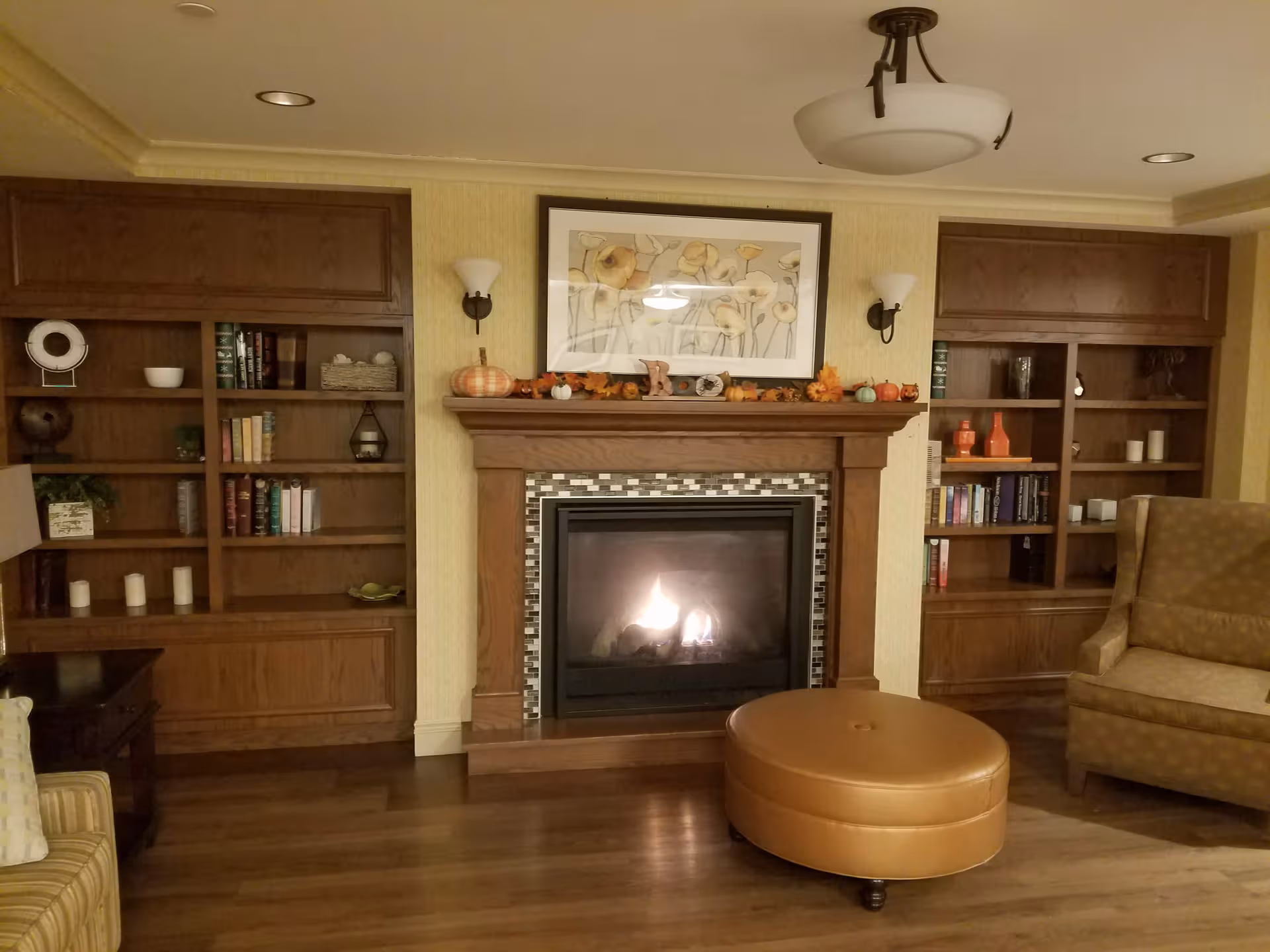 Cozy senior living room with lit fireplace, wooden bookshelves, and plush seating.
