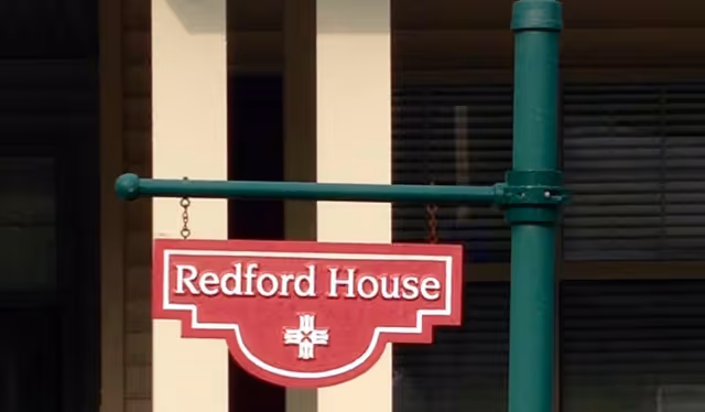A red hanging sign reading "Redford House" mounted on a green post in front of a building.