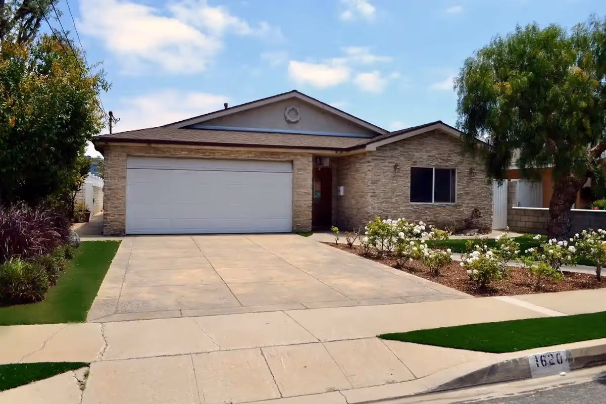 Front exterior of a single-story stone house with a two-car garage and landscaped yard.