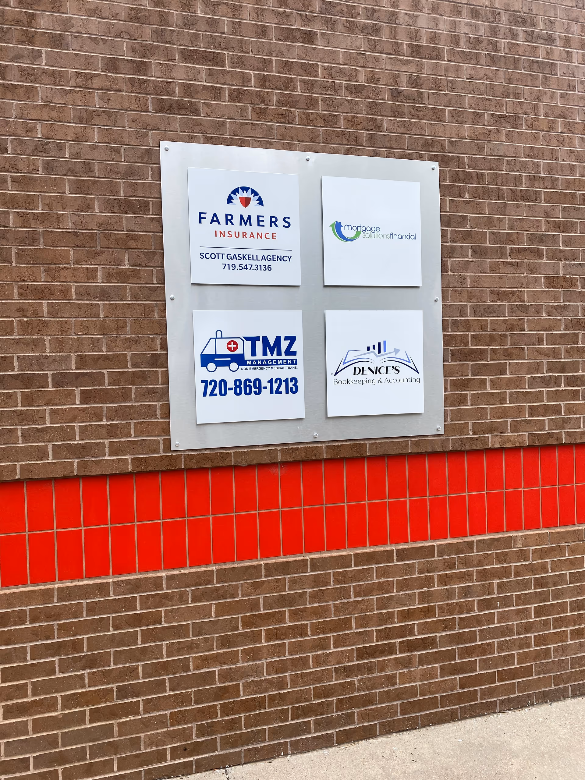 Brick building exterior with a four-panel sign displaying multiple business logos.