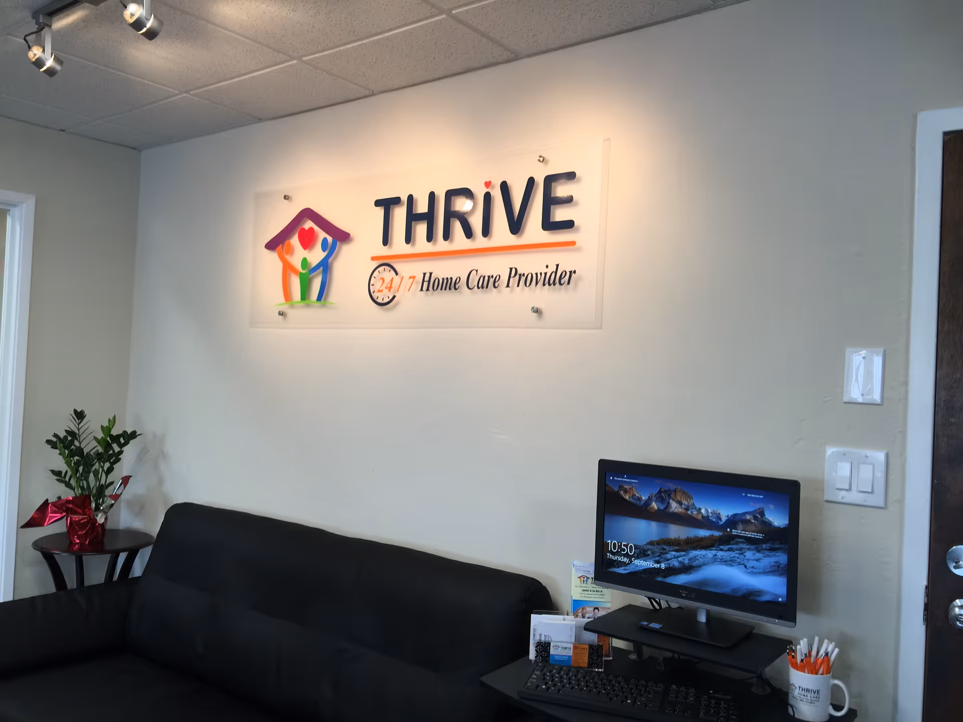Reception area shows Thrive Home Care sign, computer desk, and black couch.