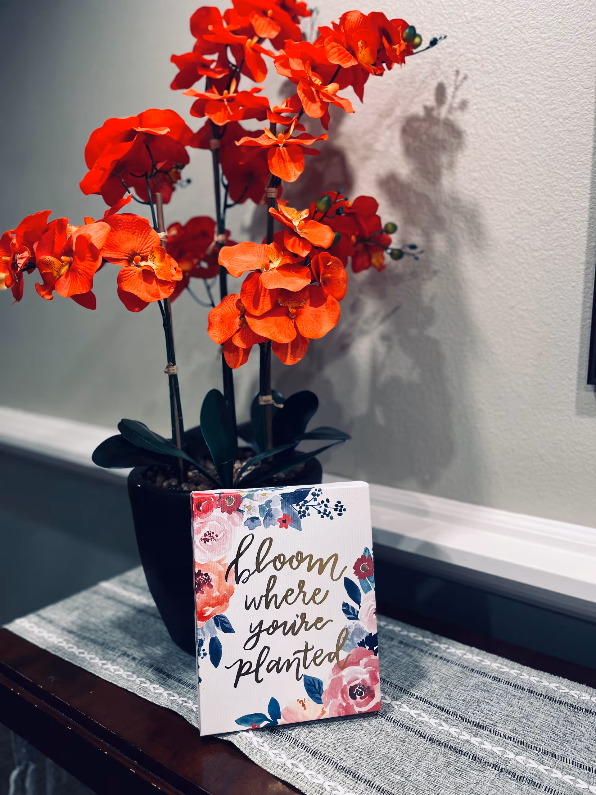 Bright orange blossoms in a pot beside a decorative card on a table indoors.