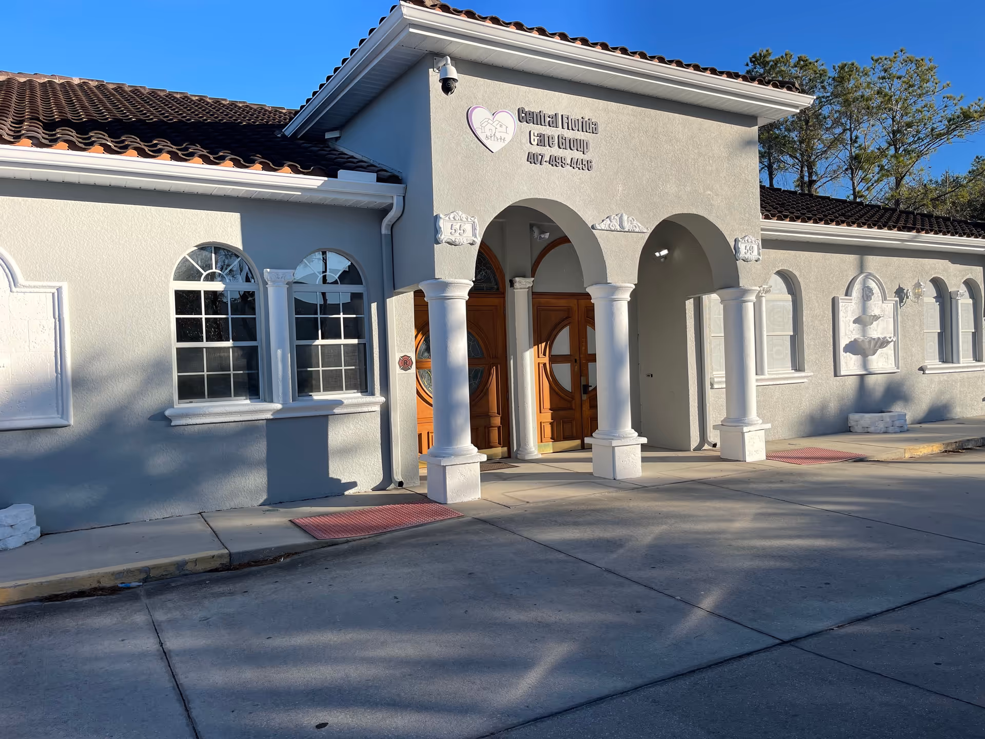 A pale gray senior care facility entrance with arched columns and double wooden doors.
