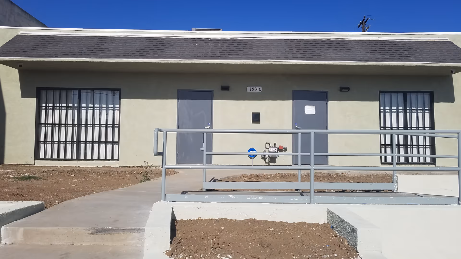 Front view of a beige facility with two grey doors, barred windows, and a ramp.
