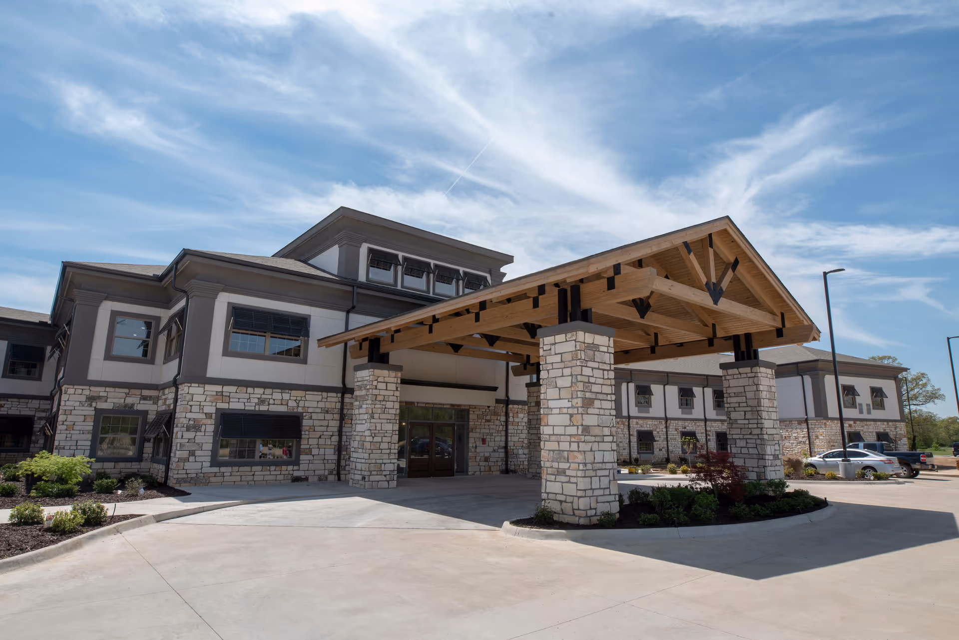 Exterior view of a modern senior living facility with stone columns and a wooden porte-cochere.