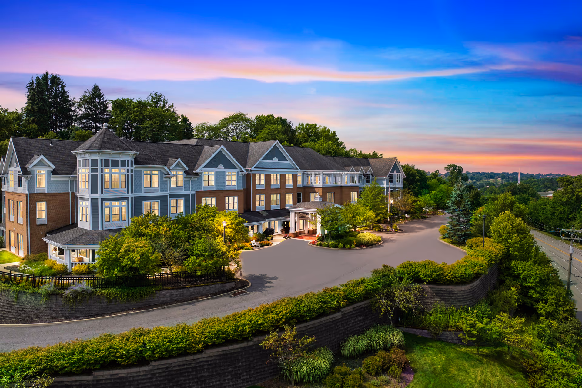 An expansive senior living facility with a curved driveway and landscaped grounds at sunset.