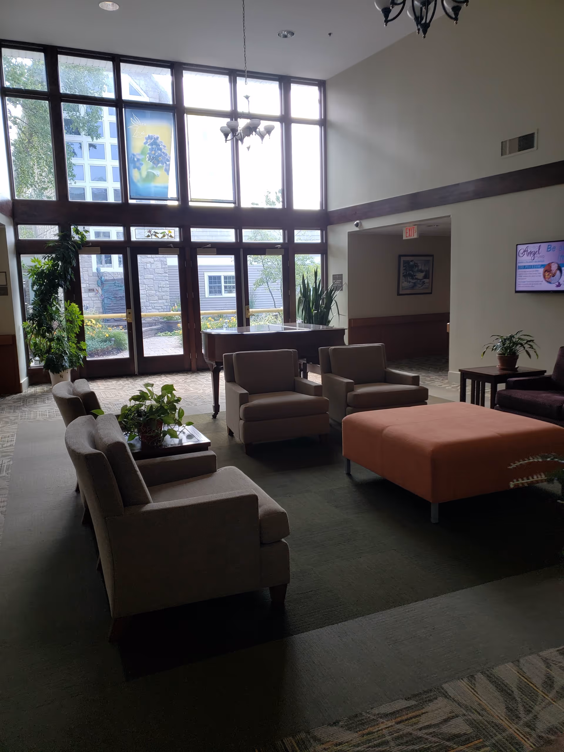 Bright lobby seating area with sofas, ottoman, plants, and a large window wall.