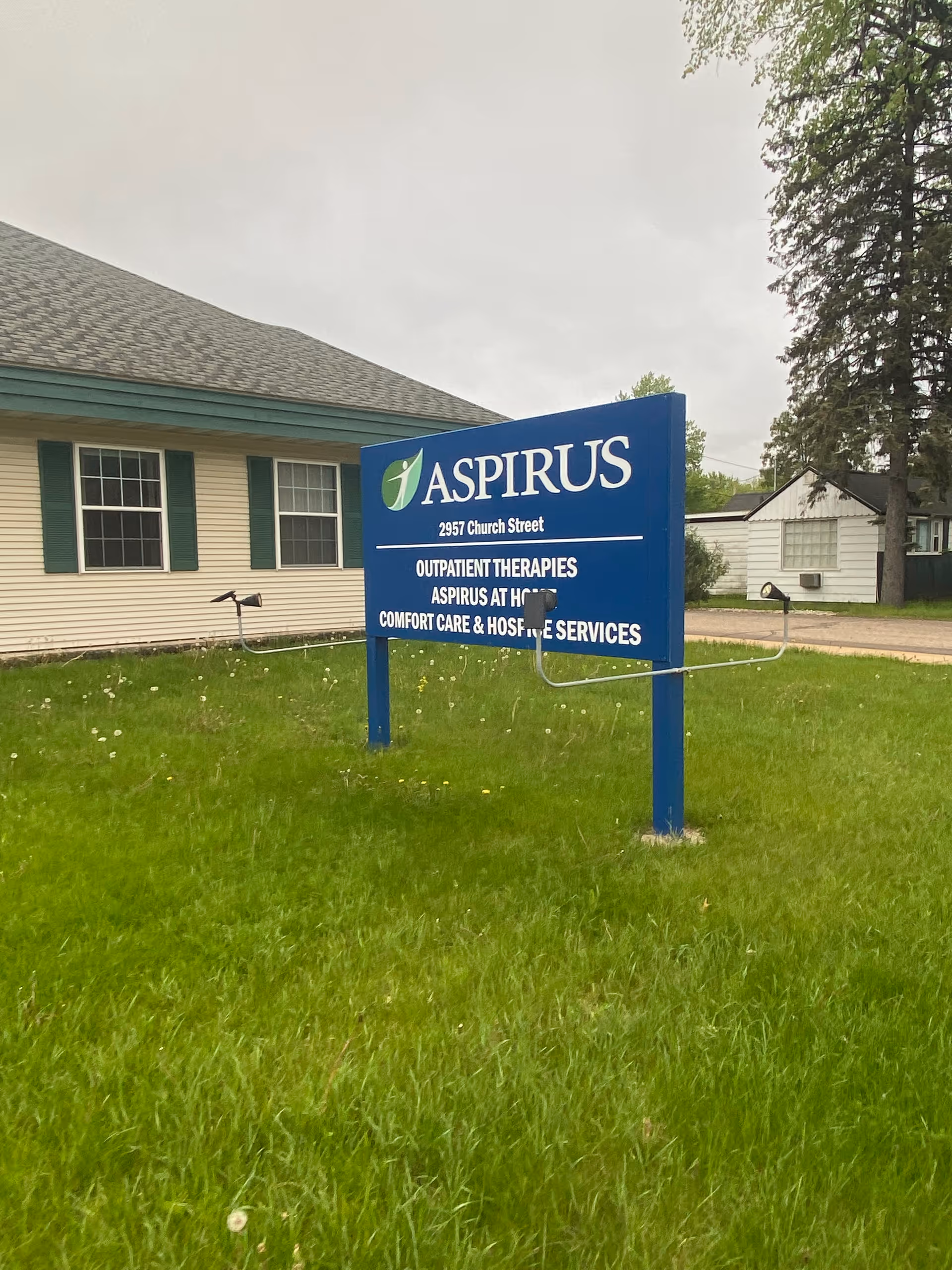 Blue Aspirus sign on a grassy lawn in front of a beige building.