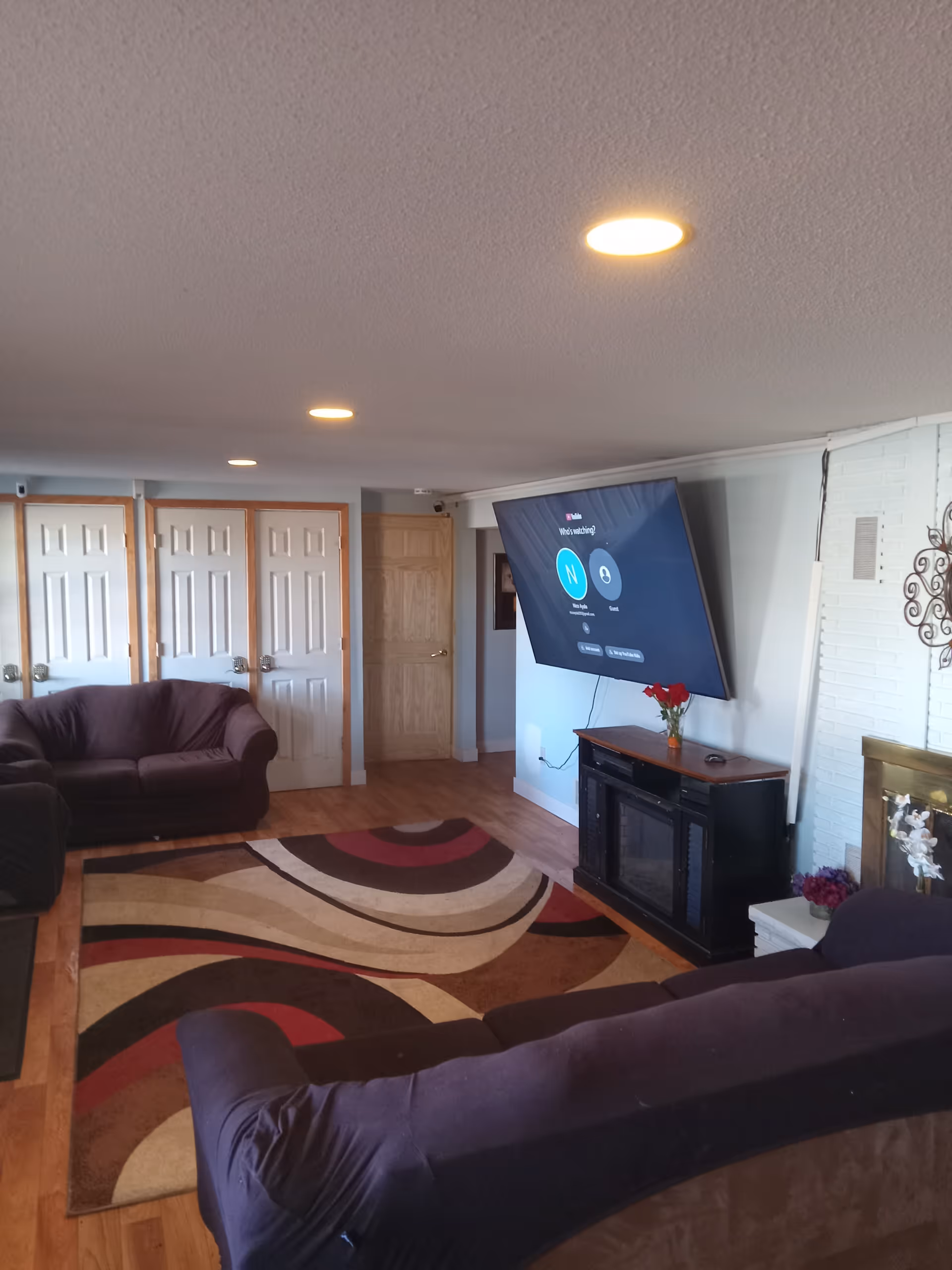 Cozy living room with purple couches, patterned rug, wall-mounted TV, and fireplace decor.