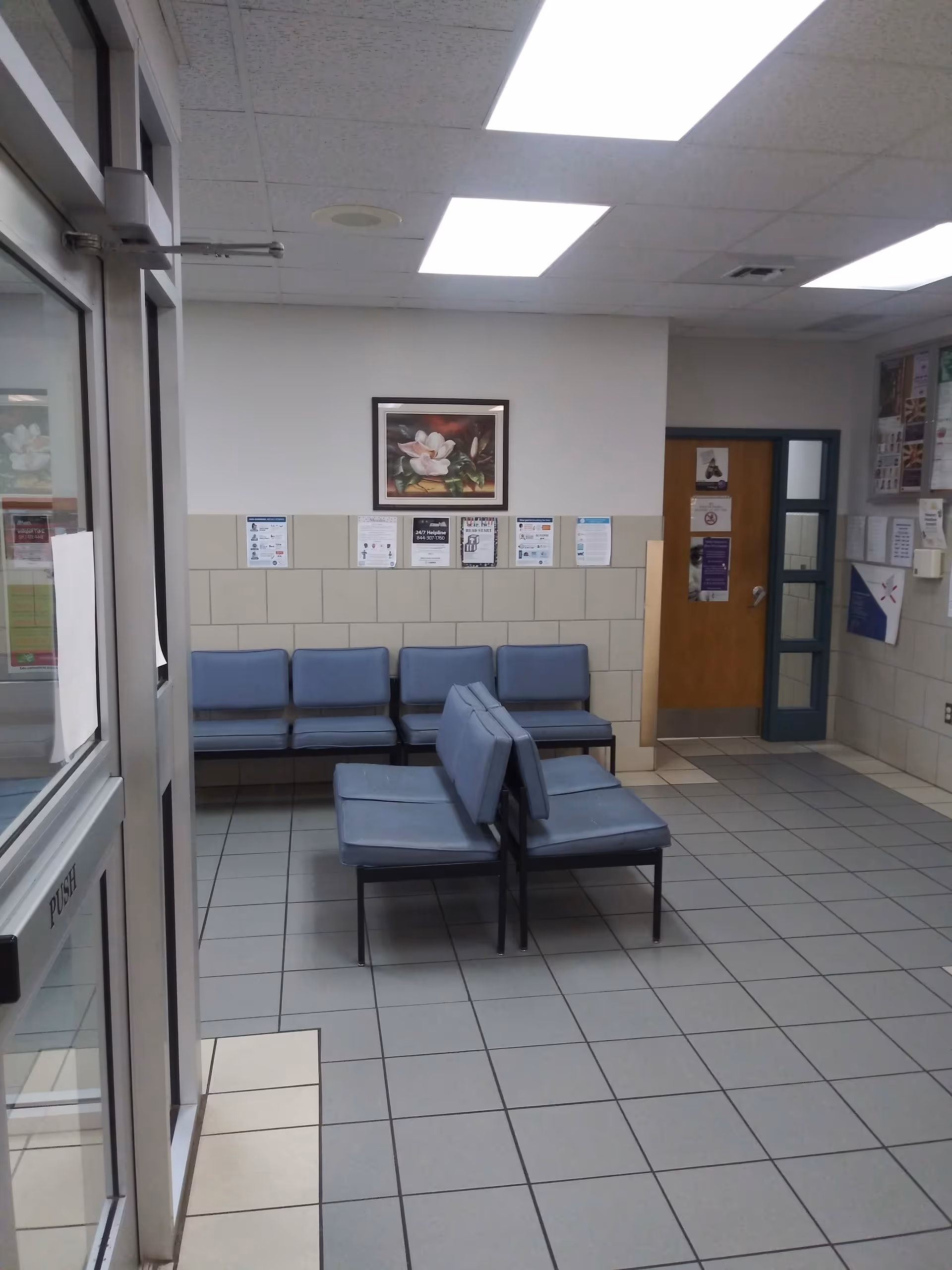 Waiting area with blue chairs and tiled floor in a hall.