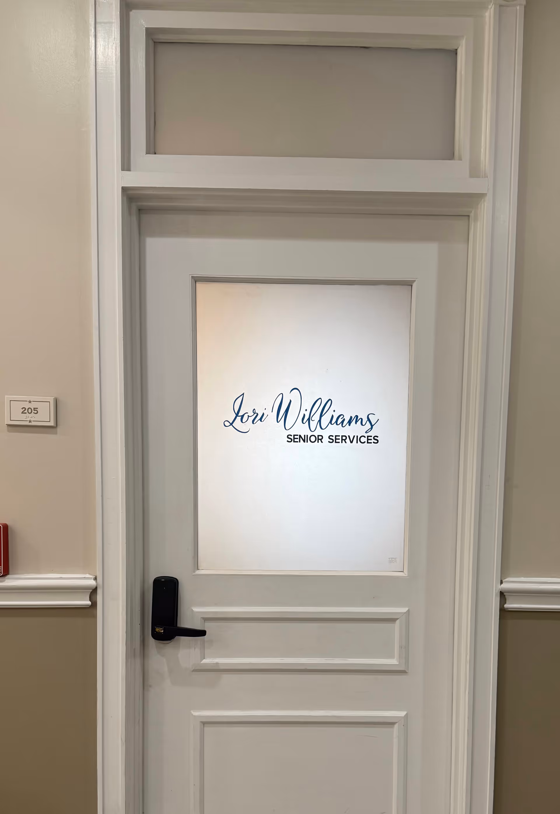 White interior door with frosted glass panel reading Lori Williams Senior Services.
