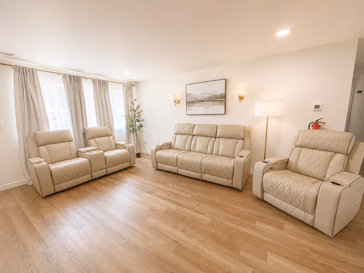 Spacious beige living room with recliner chairs, a sofa, and large windows.