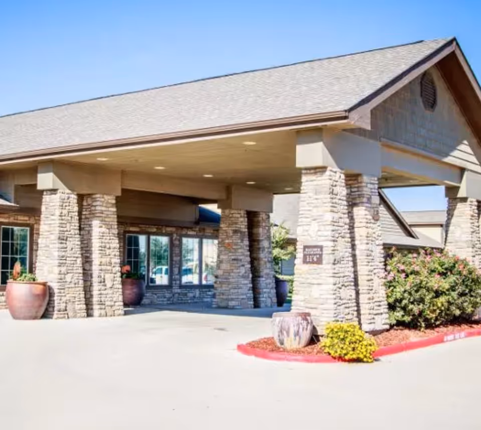 The exterior entrance of Legacy Ranch senior living facility featuring a covered area with stone pillars and plants.