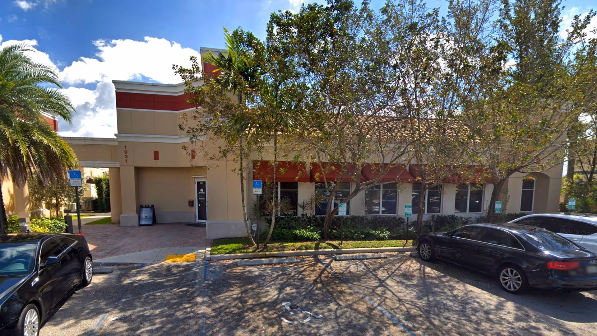 Exterior view of a senior care facility with a parking lot and trees.