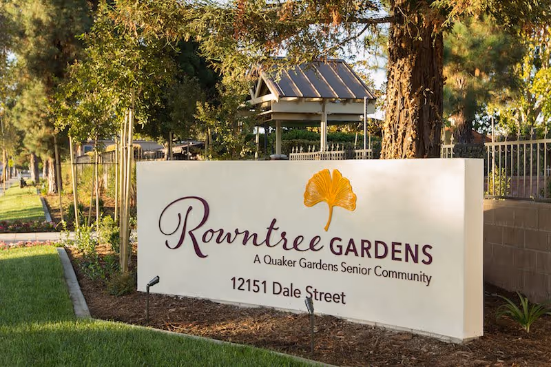 A large sign reading Rowntree Gardens in front of a landscaped senior living campus.