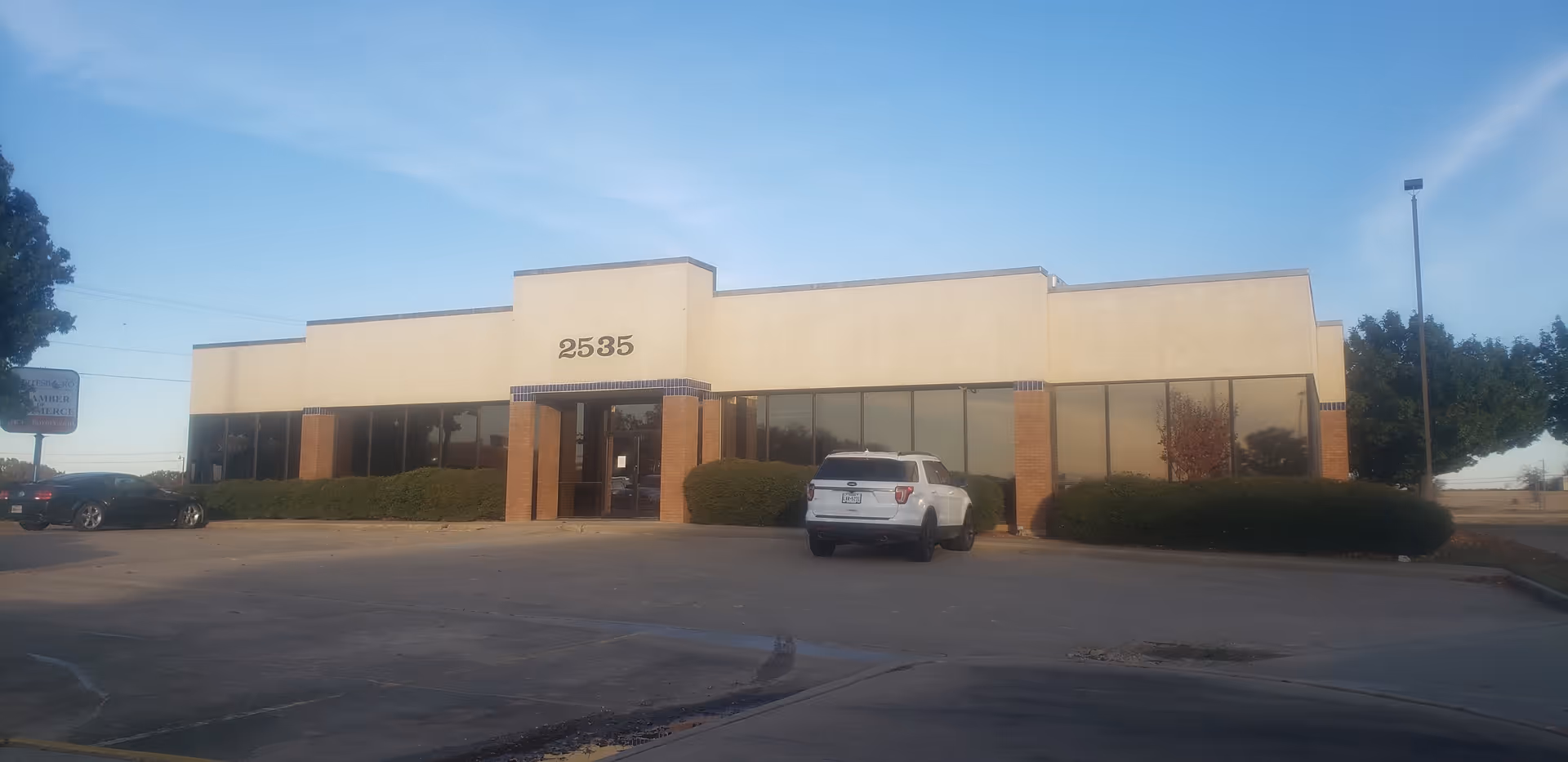 Front view of a single-story beige commercial building with large glass windows and a parking lot.