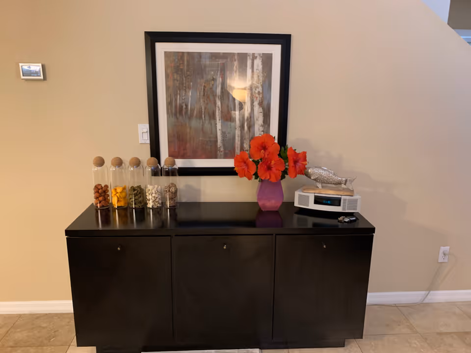A dark cabinet against a beige wall with jars, red flowers, and framed artwork.
