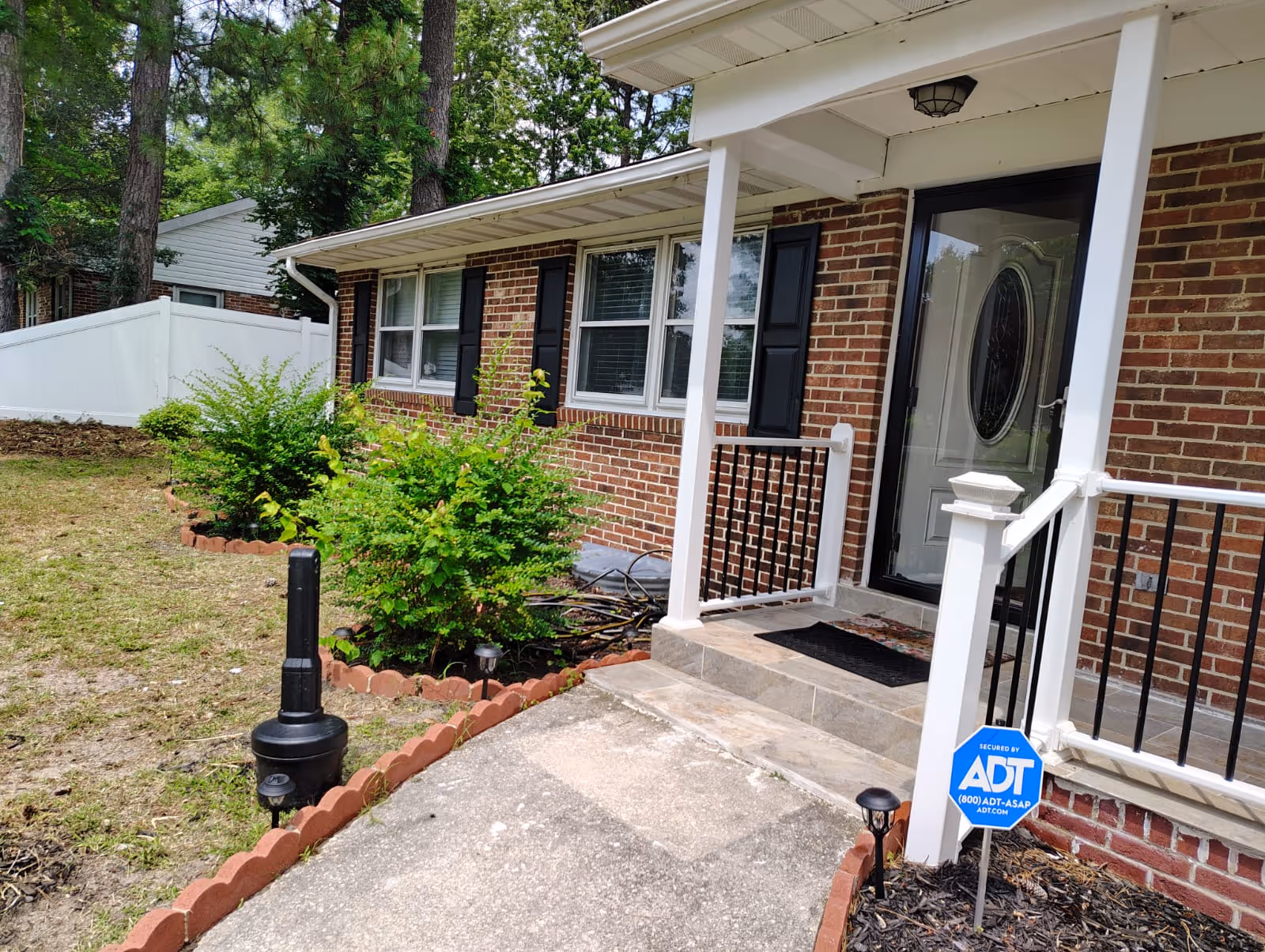 Exterior of Auldin Assisted Living front entrance with brick facade, white porch railing, and landscaping.