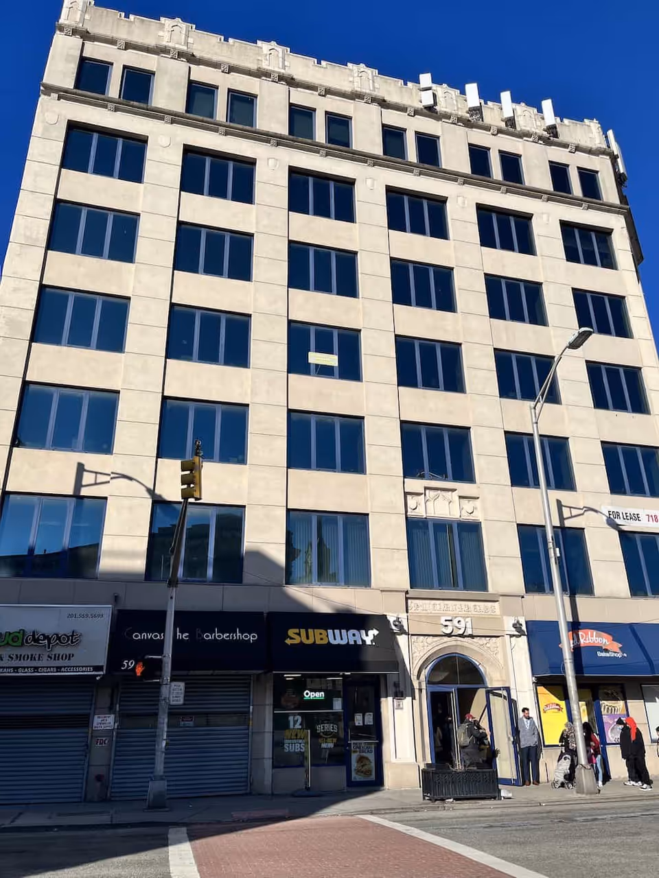 Tall beige urban building with many windows and Subway storefront at street level.