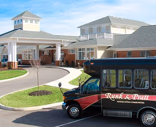 Front entrance of a senior living facility with a covered porte-cochere and a Runk & Pratt shuttle bus parked outside.