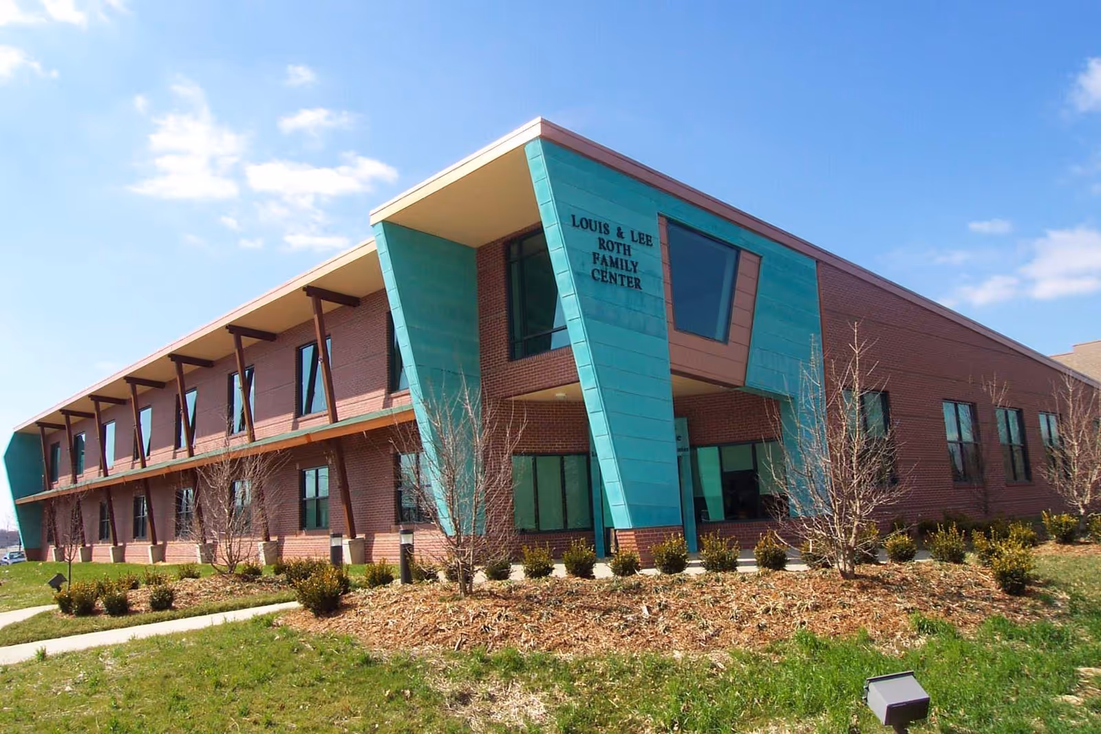 Exterior view of a brick facility with a teal architectural column and landscaping.