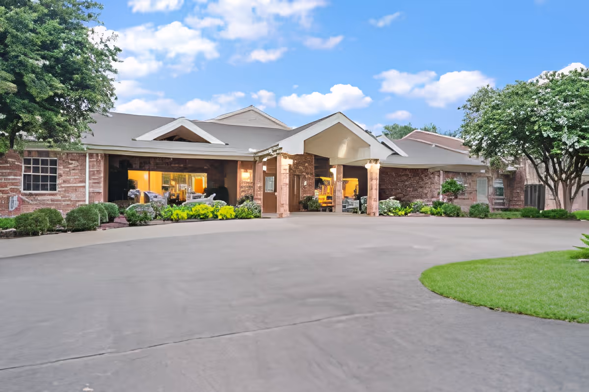 Front exterior of a single-story senior living building with a covered entrance, circular driveway, and landscaped greenery.