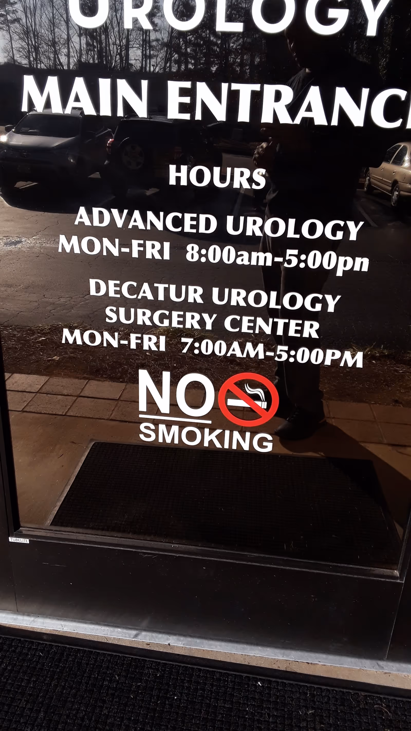 Glass entrance door with large white text advertising urology hours and no smoking.