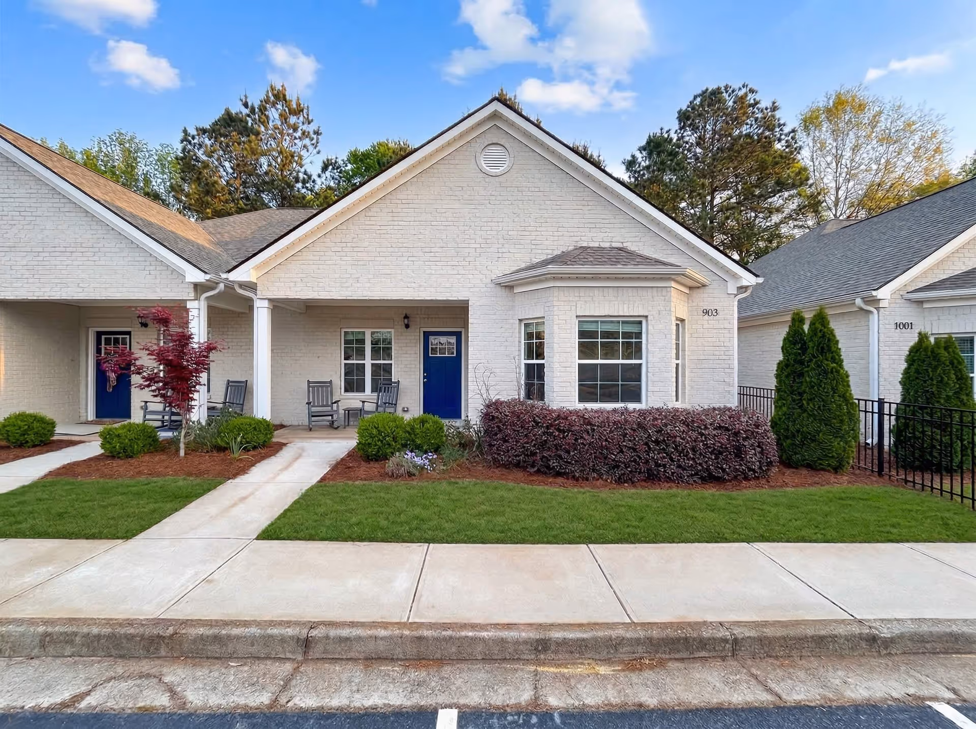 White brick senior living building with blue doors, porches, and manicured shrubs.