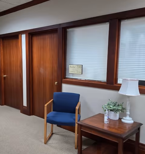 Interior hallway in a senior living facility with blue chair, side table, and suite sign.
