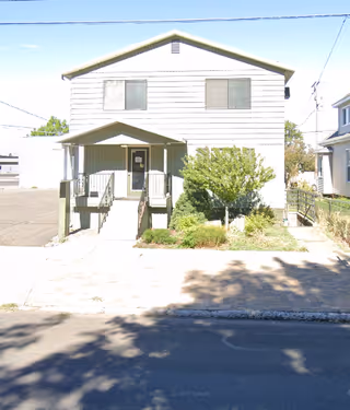 Front exterior of a two-story building with a small entrance porch and shrubs.