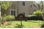 Front view of a two-story beige senior living building with a lawn and address sign.