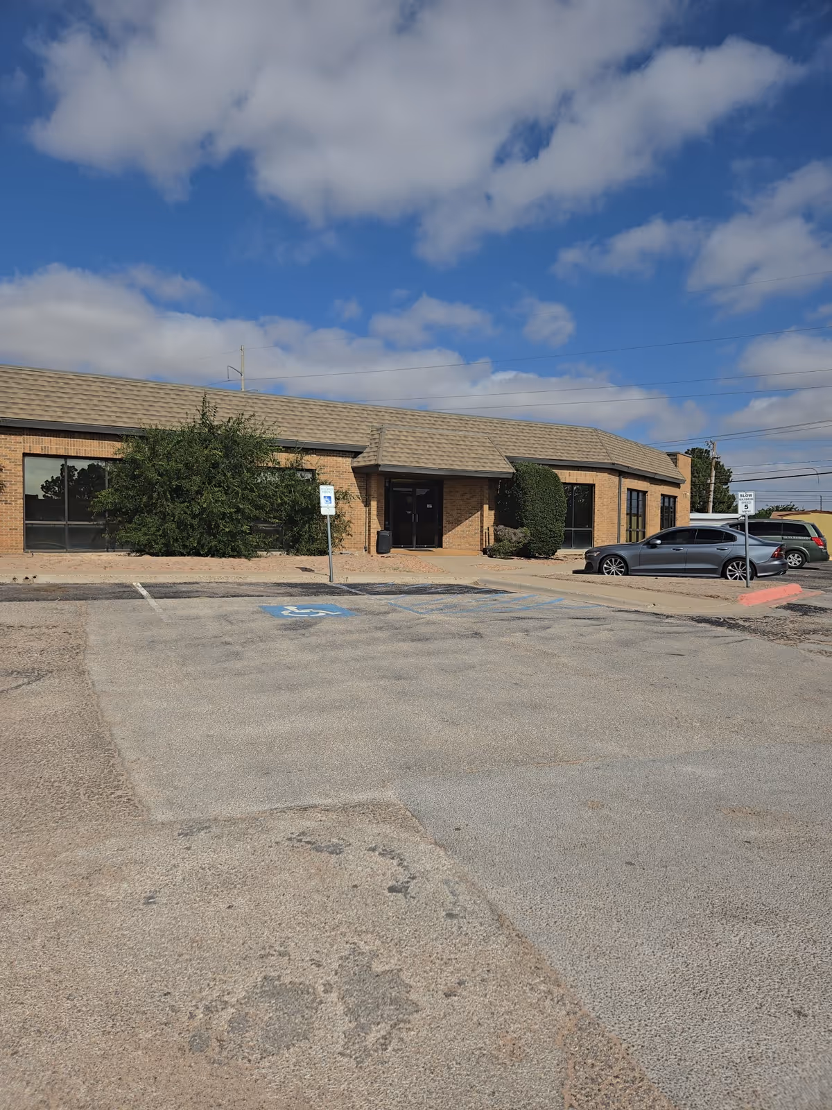Brick single-story facility exterior with parking lot and handicap accessible space in foreground.