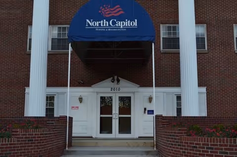 Brick building entrance with white columns and a blue North Capitol Nursing and Rehabilitation awning.