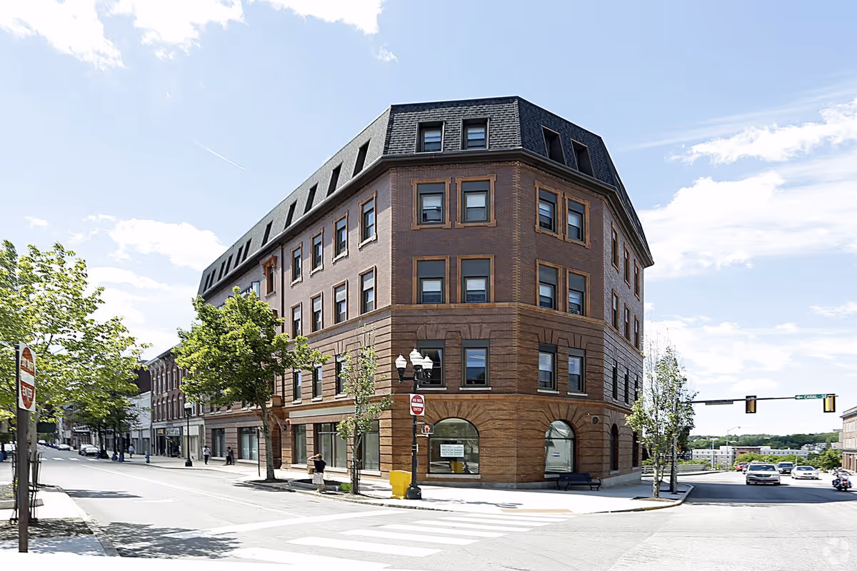 Brick corner building on a sunny street with trees nearby.