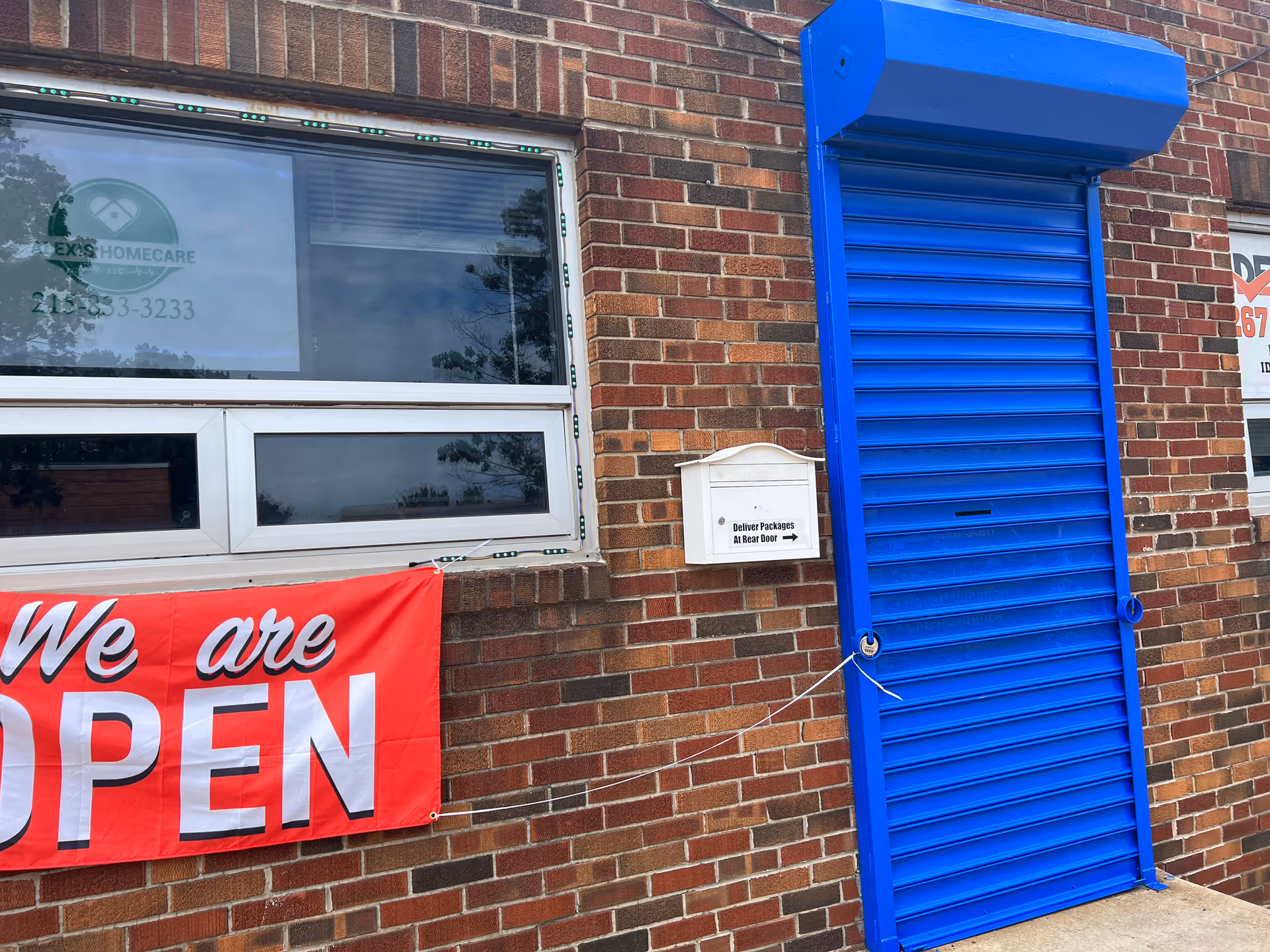 Brick building exterior with a bright blue door and a 'We are OPEN' banner.
