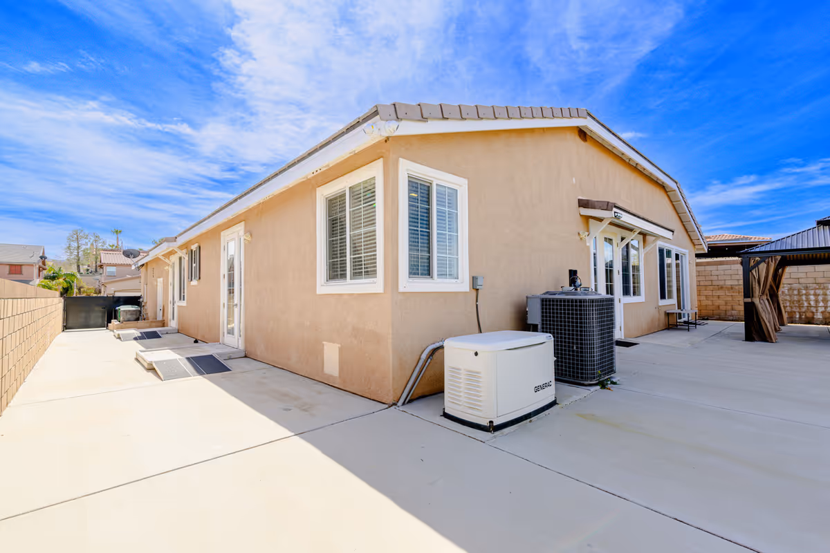 Back exterior of a single-story beige house with concrete patio and HVAC unit.