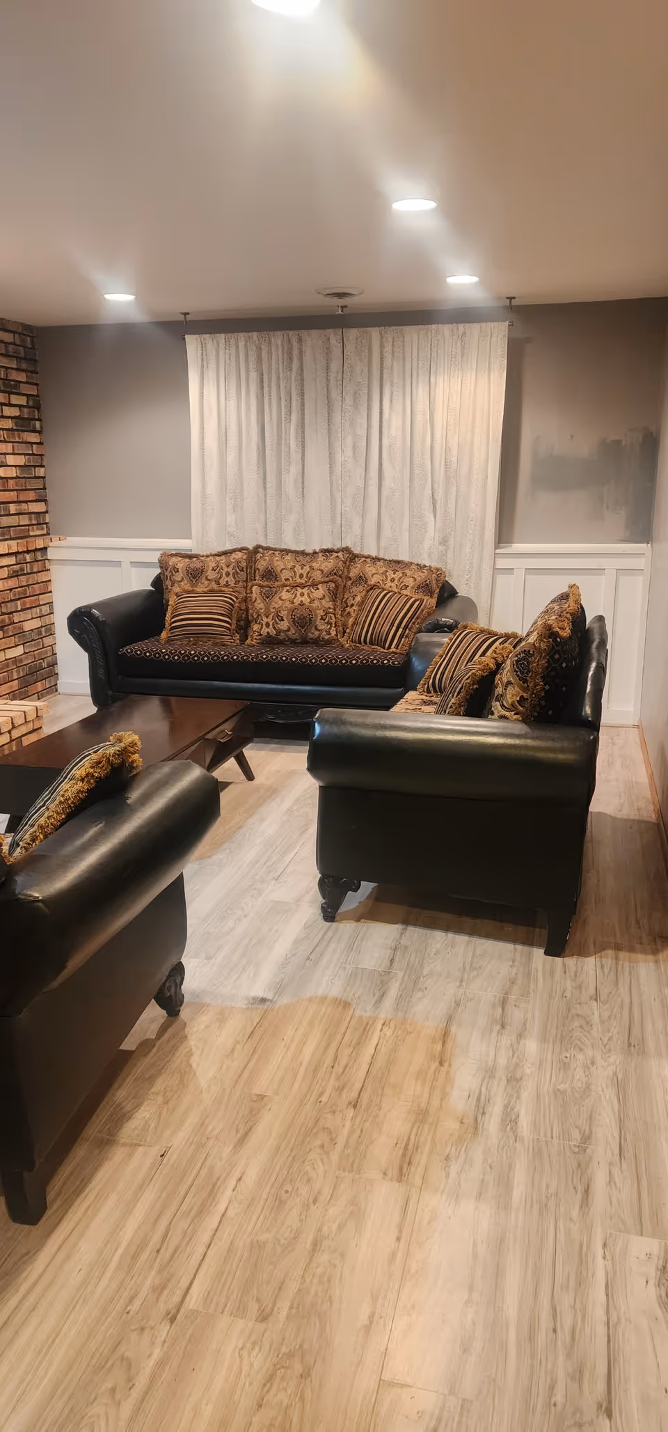 Cozy senior living facility living room with black leather sofas, patterned cushions, and curtains.