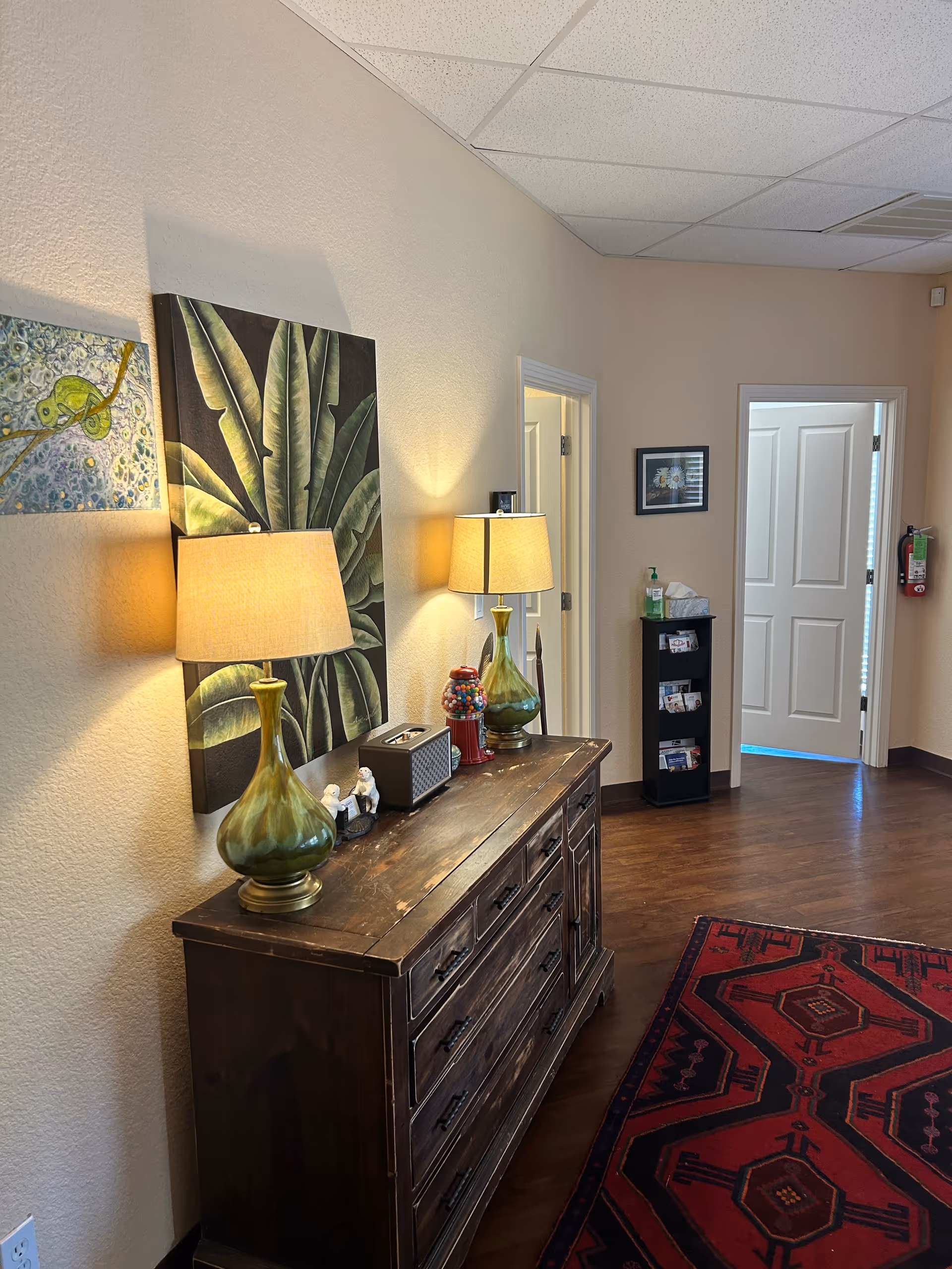 Interior hallway with a wooden dresser, lamps, wall art, and a red patterned rug.