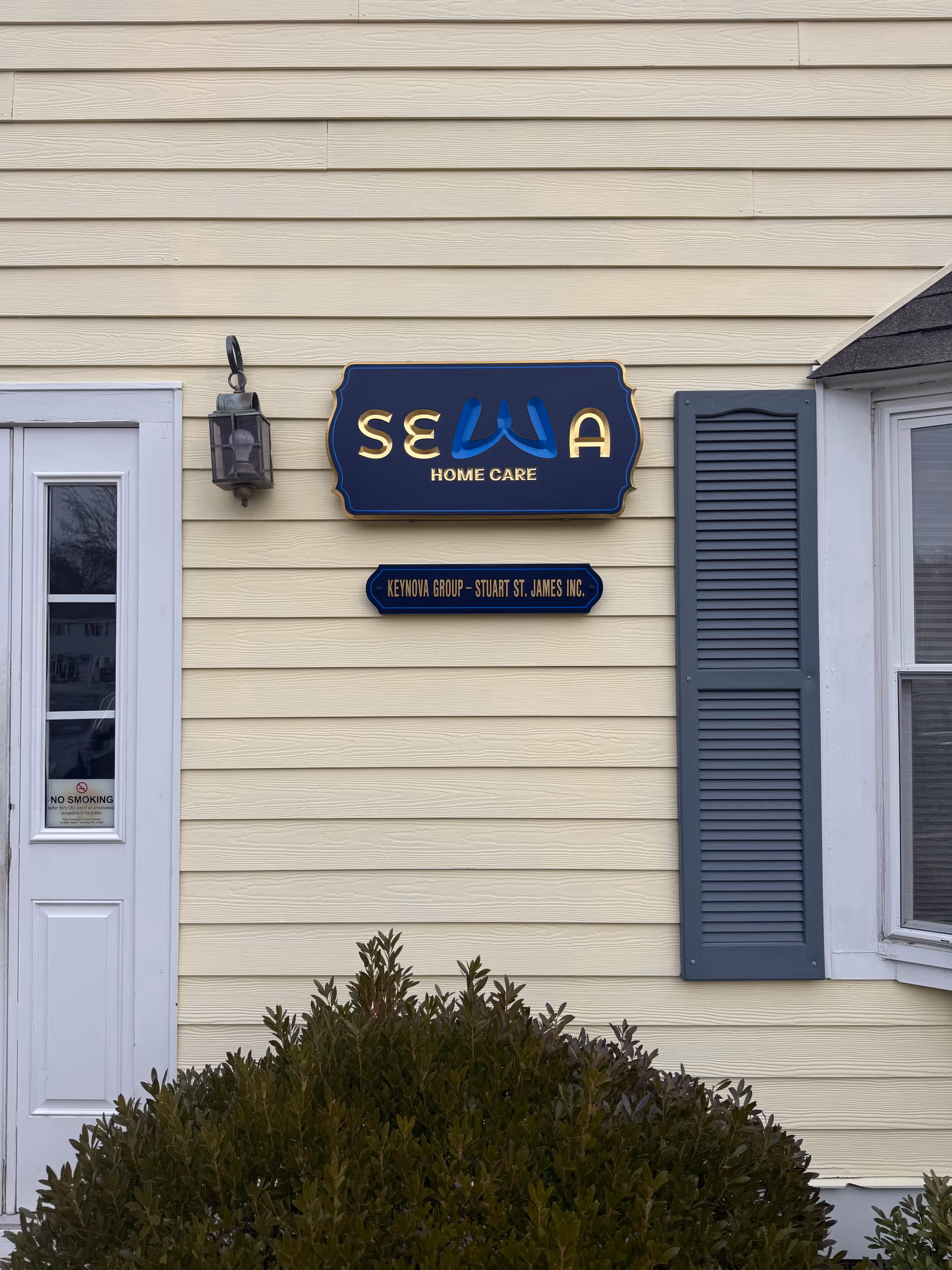 Exterior view of SEWA Home Care building with sign and shrubbery.