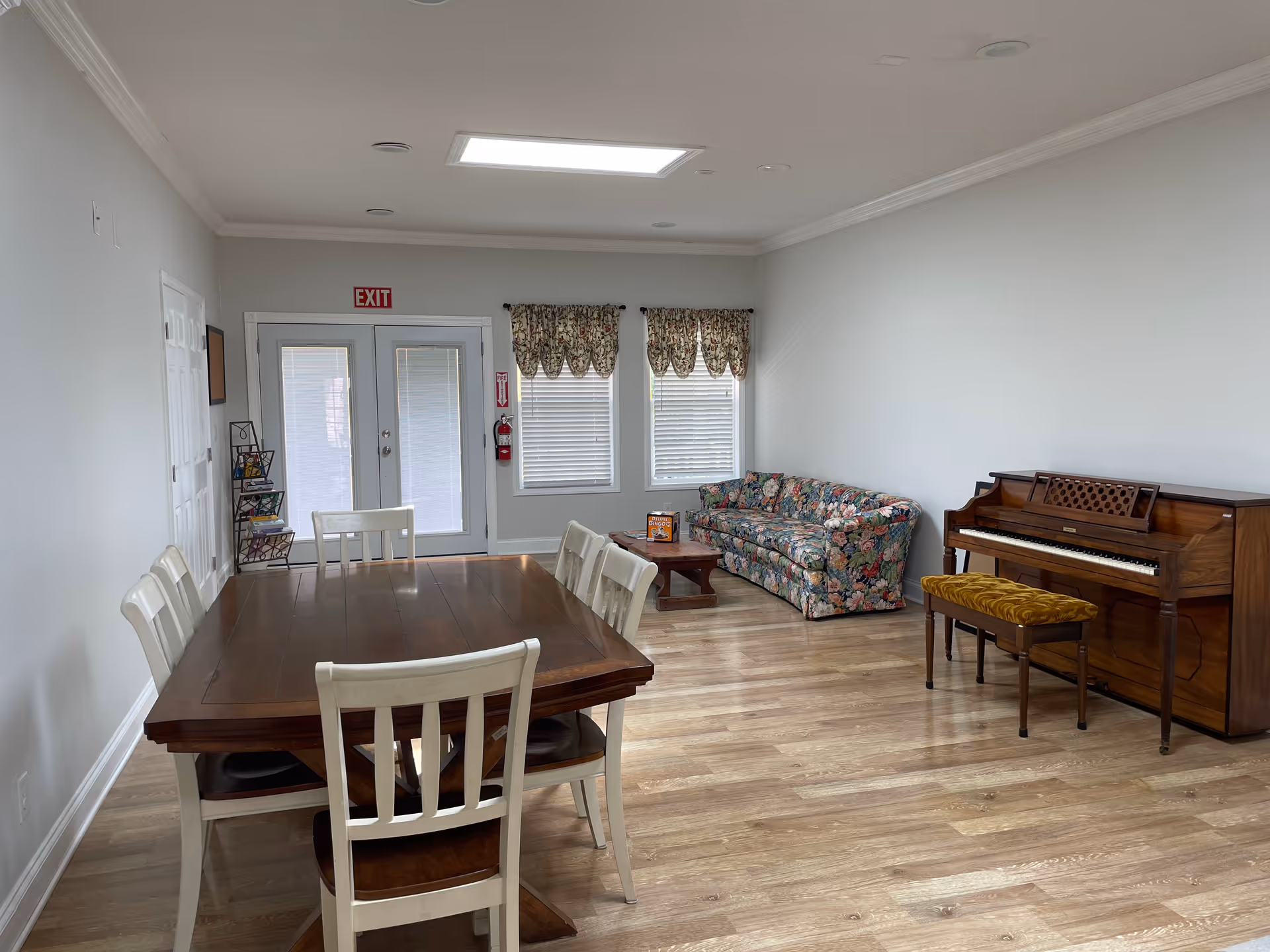 Interior common area with a large wooden dining table, floral sofa, and piano.